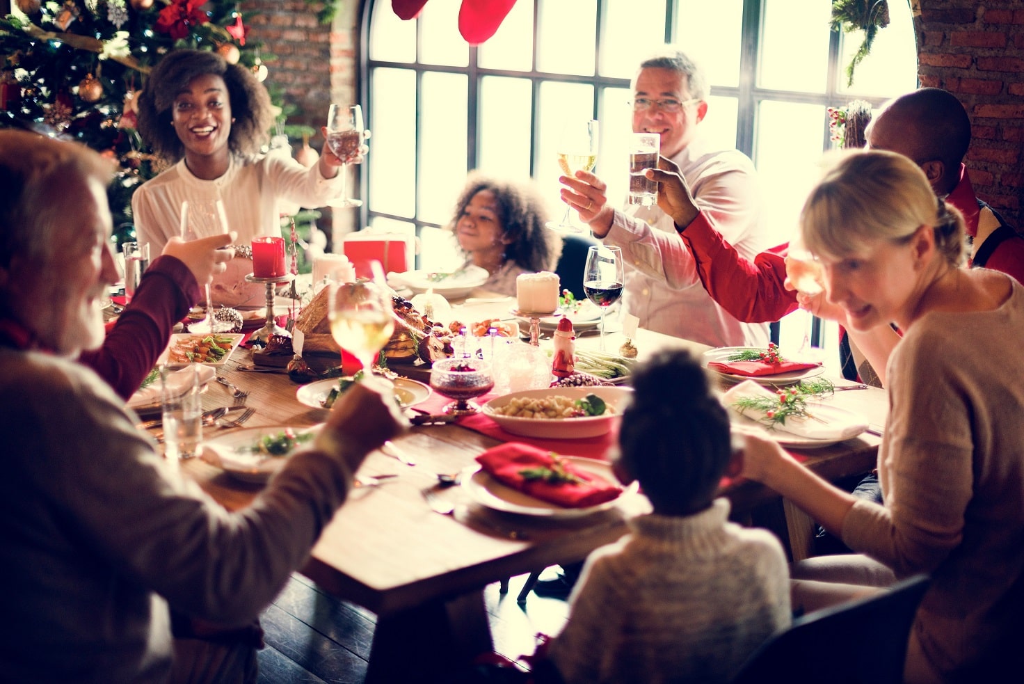 A family sits around a holiday table, smiling and cheers-ing their glasses.
