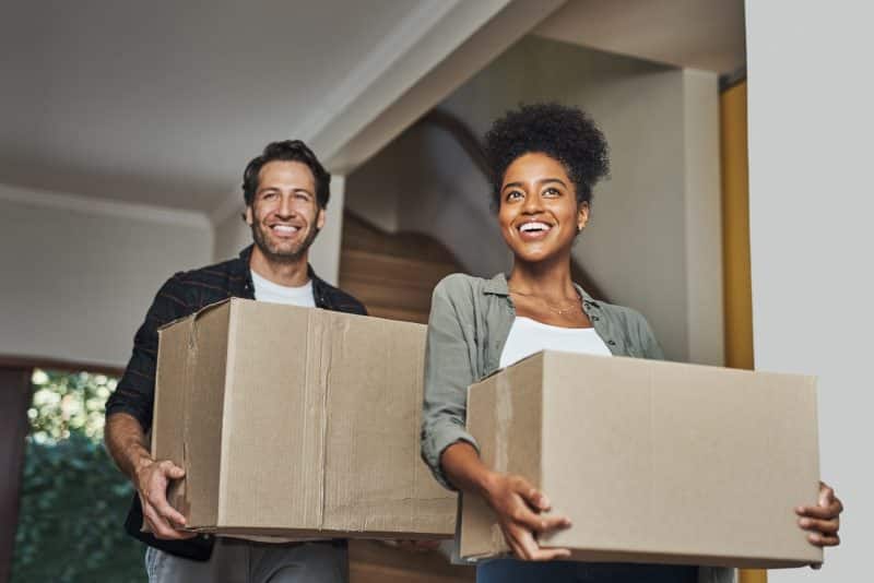 A couple holds boxes and moves into their new home.