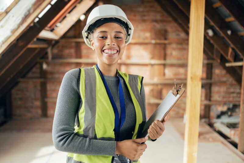 A smiling construction worker holds a clipboard.