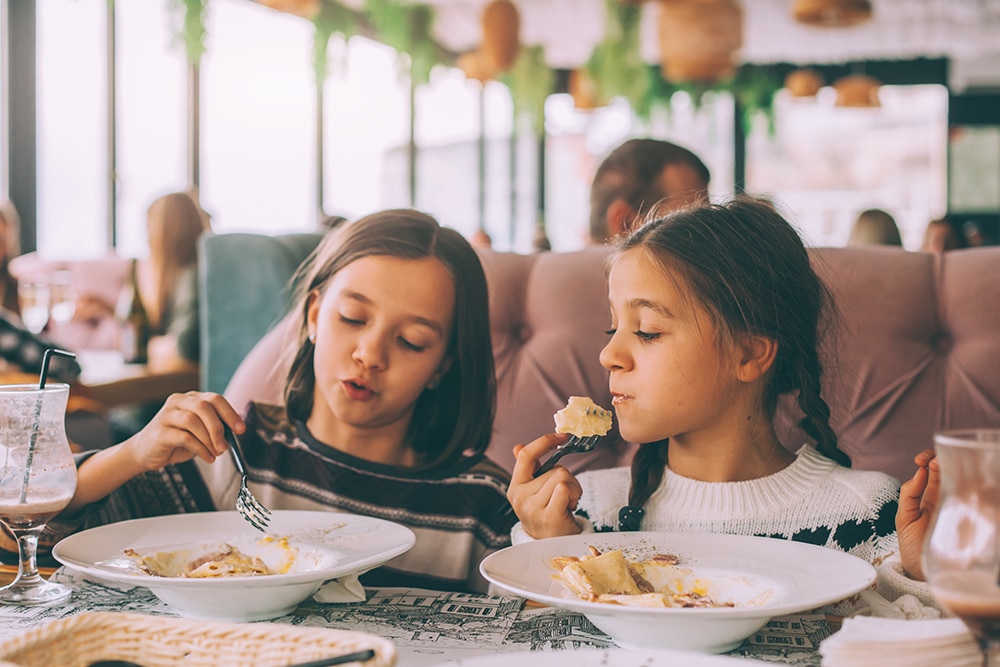 Two children enjoying a pasta dishes in a restaurant / Deux enfants dégustant un plat de pâtes dans un restaurant