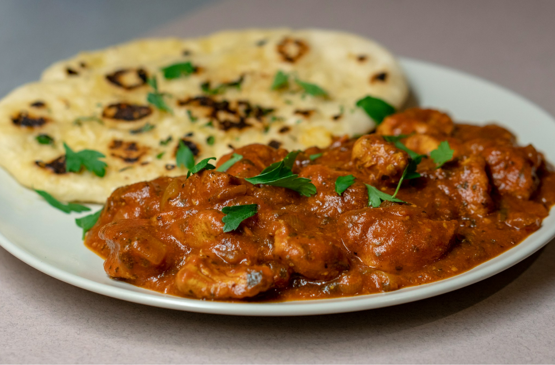 A close up of butter chicken and naan on a plate. Gros plan sur du poulet au beurre et du naan dans une assiette.