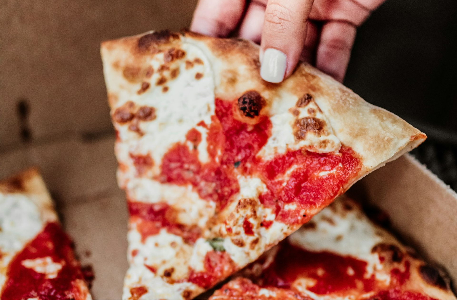 A close up of someone pulling a slice of pizza out of a takeout box. Gros plan sur quelqu’un qui sort une tranche de pizza d’une boîte à emporter.