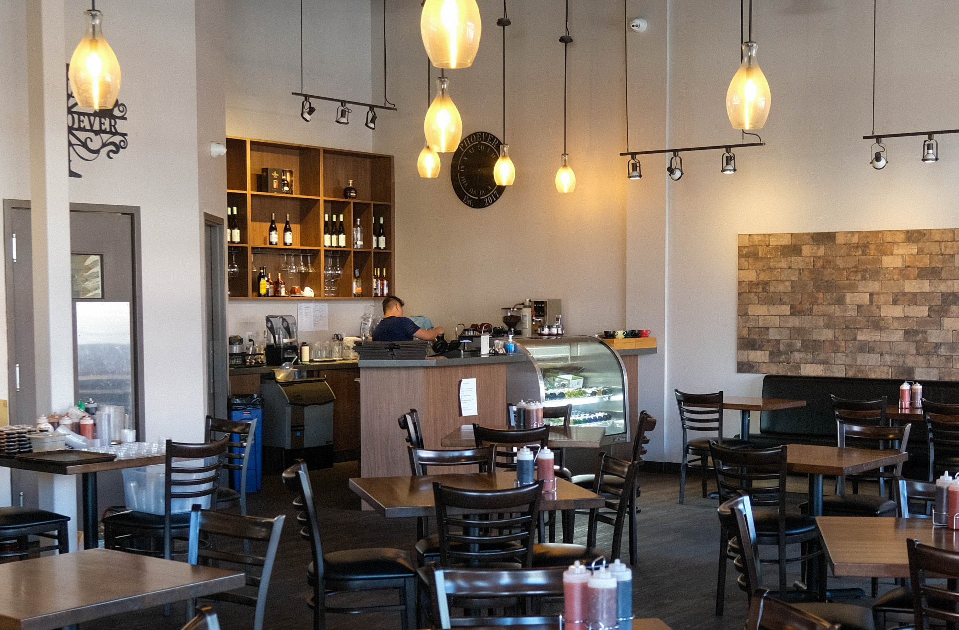 The interior of PhoEver Noodles, showing plenty of seating, and a worker behind the counter making tea. L’intérieur du restaurant PhoEver Noodles, avec de nombreux sièges et un employé qui prépare du thé derrière le Comptoir.