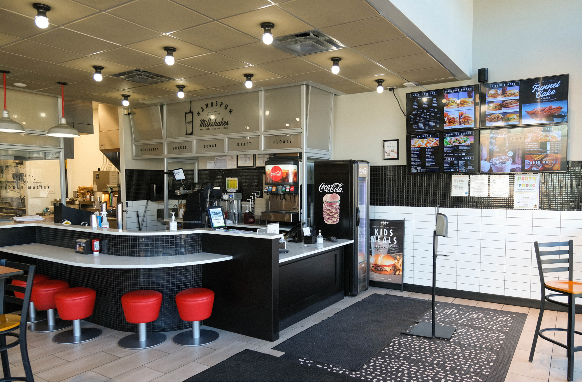 The interior of Wayback Burgers in Griesbach, showcasing the nostalgic décor with a bar to eat at with bright red bar stools. L’intérieur du Wayback Burgers à Griesbach présente un décor nostalgique et un bar aux tabourets rouge vif où prendre une bouchée.