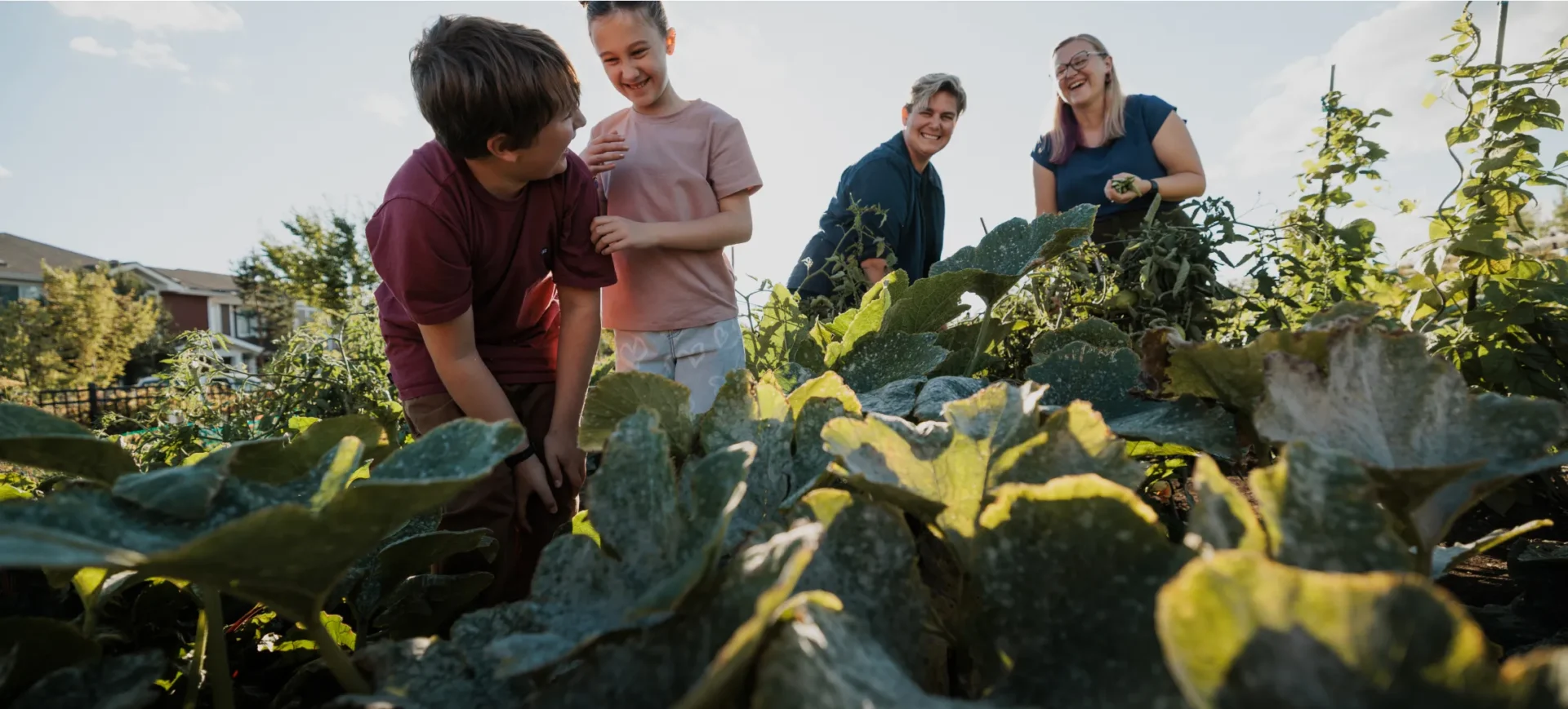 Two children and parents smiling and laughing while working in the Village at Griesbach community gardens